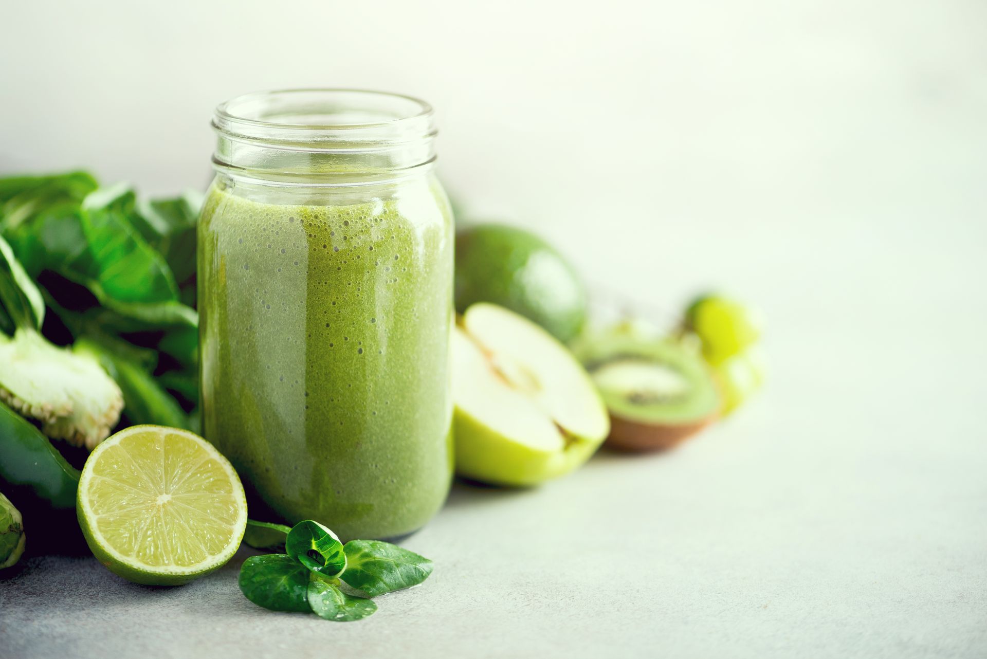 A green smoothie in a mason jar surrounded by fruits and vegetables.