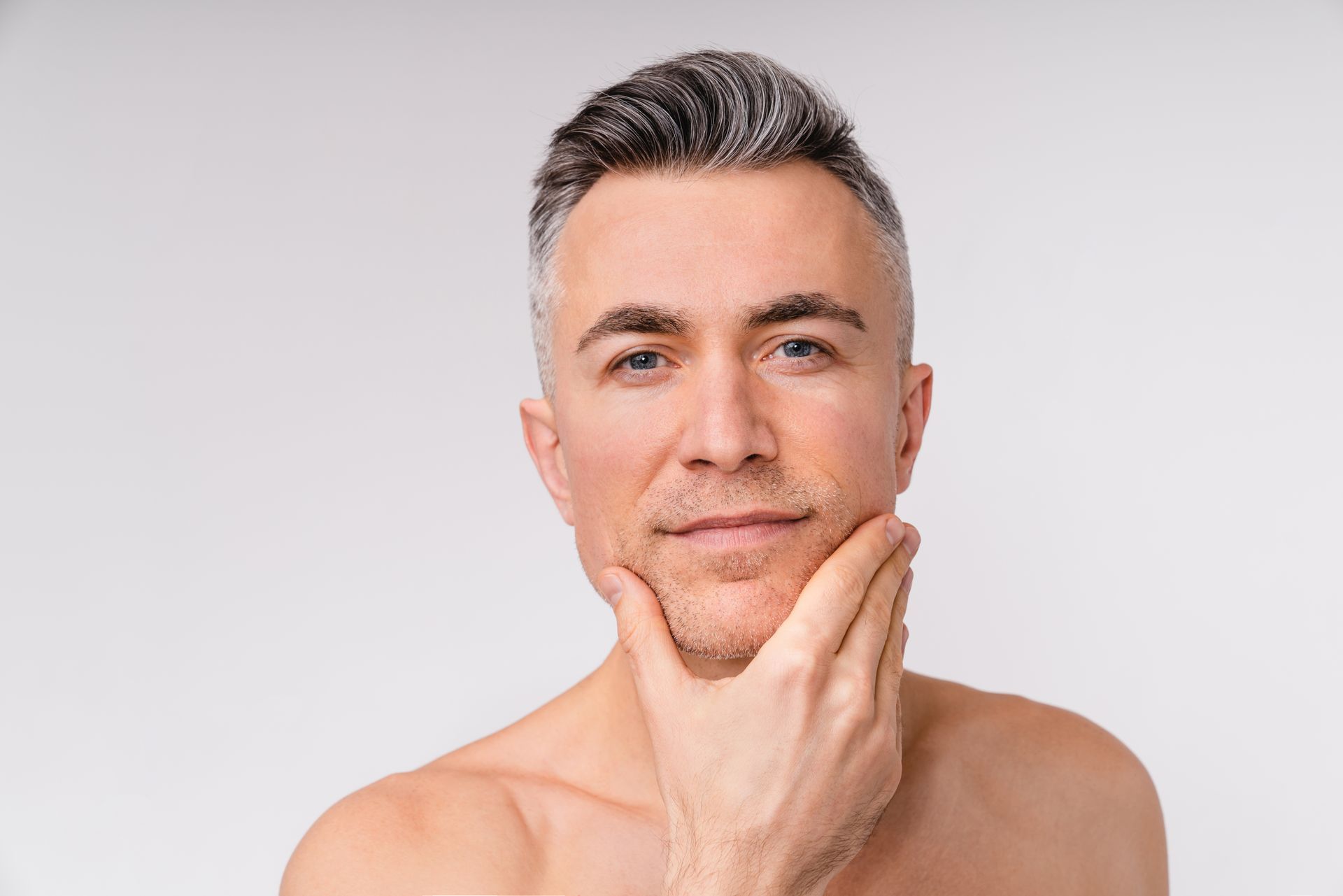 A shirtless man is holding his hand to his face.