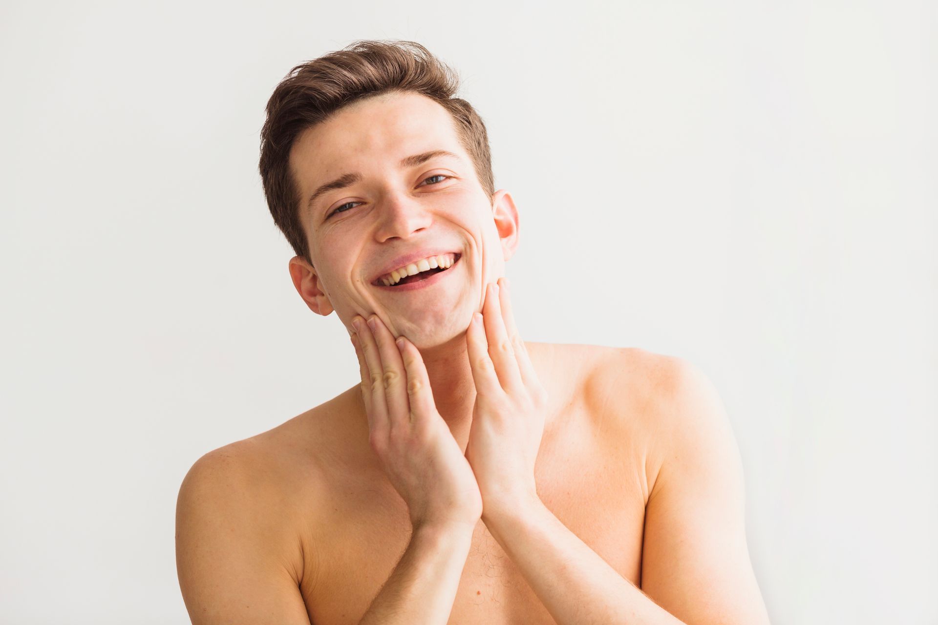 A handsome man is smiling and is touching his face with both hands