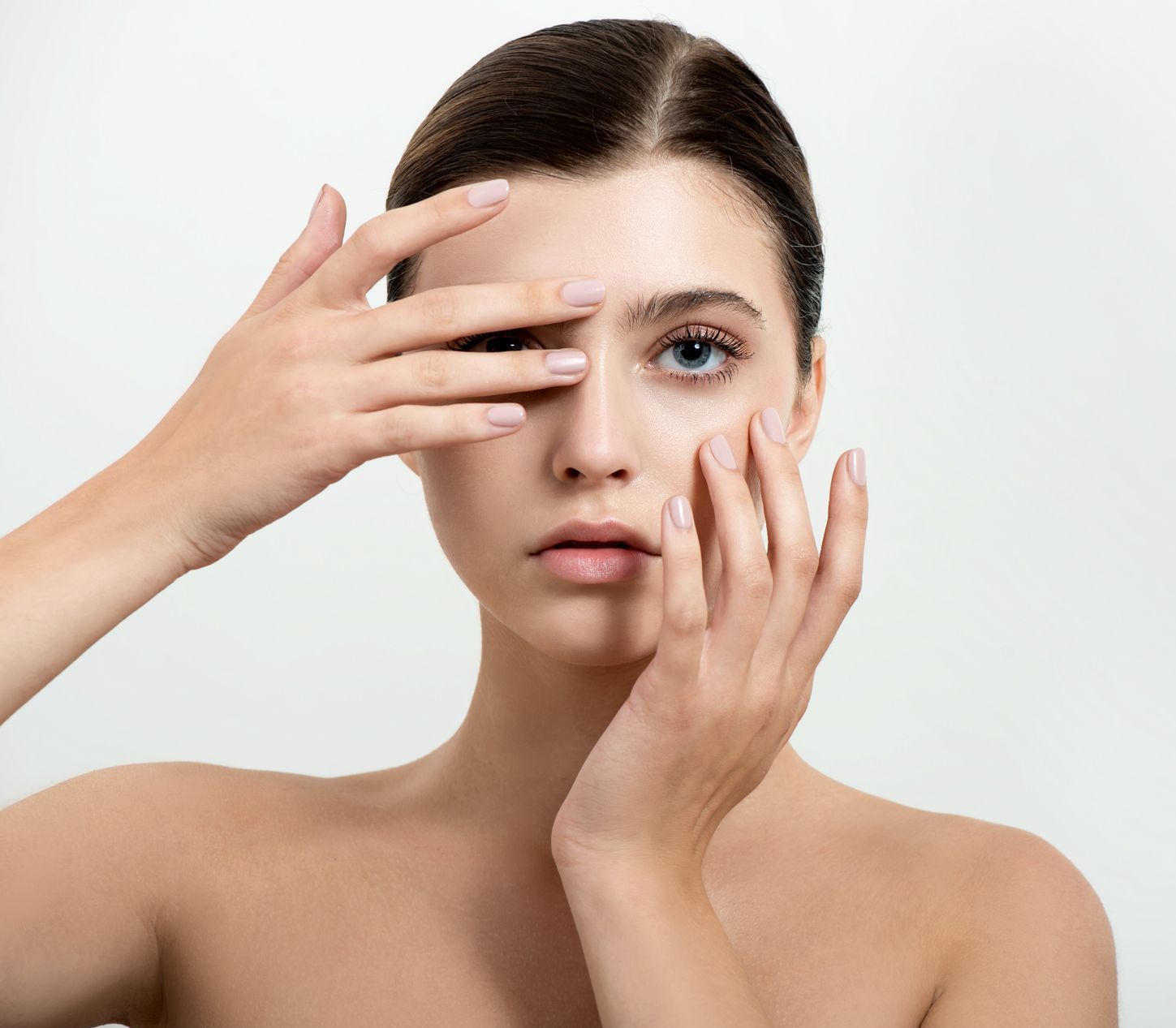Woman with fair skin and blue eyes, hands partially covering her face, looking forward with a neutral expression.