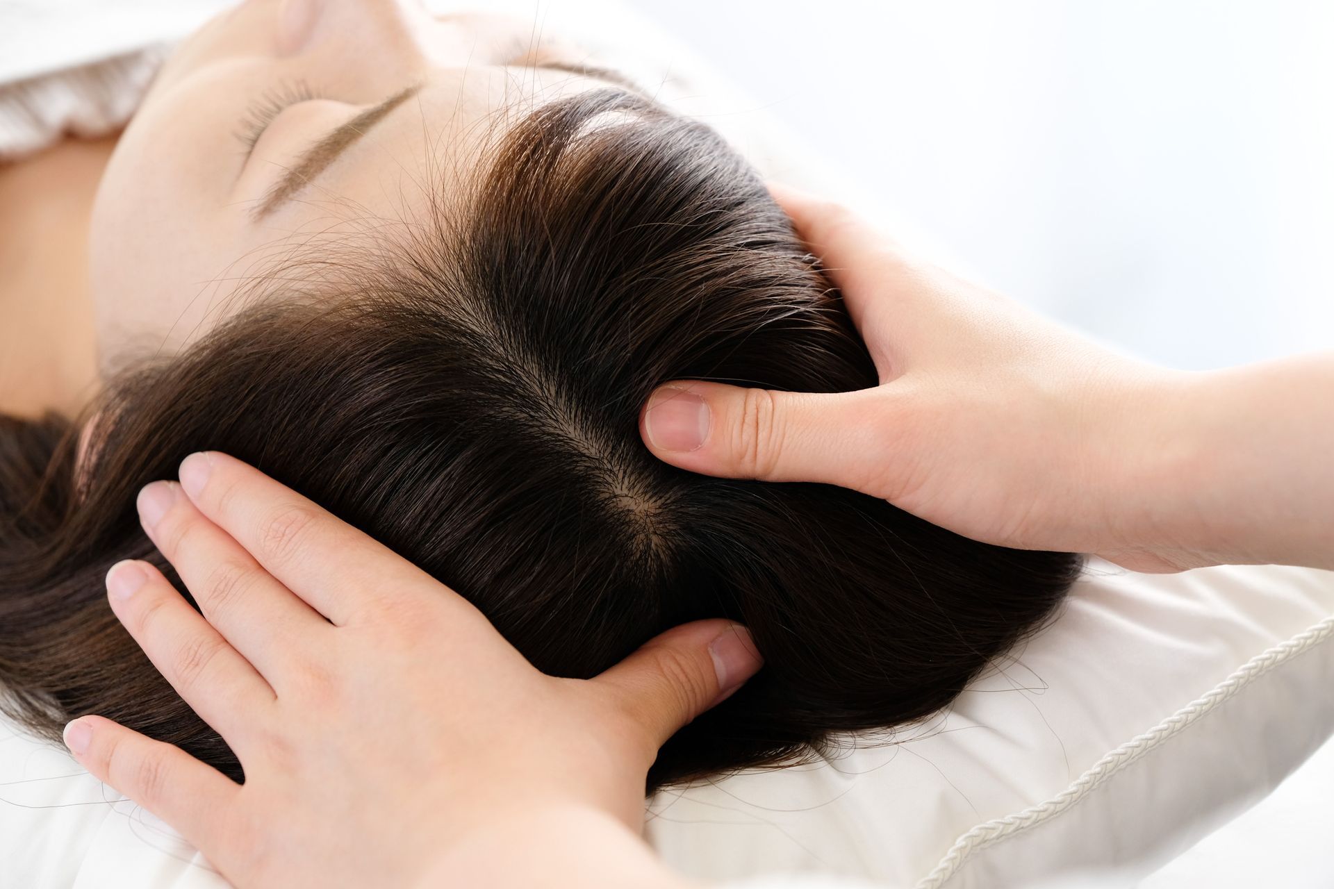 Hands massaging a person's scalp; eyes closed, dark hair, indoors.