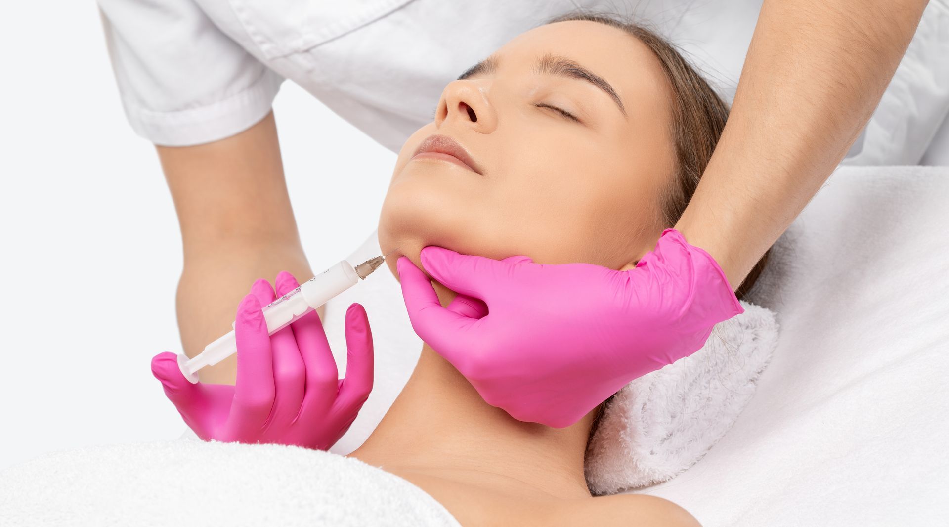 A person receiving a cosmetic injection in their jawline. Pink gloves, white background.