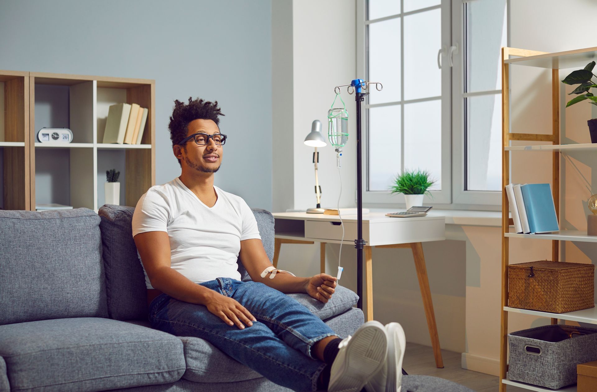 A man is sitting on a couch in a living room with an iv in his arm.