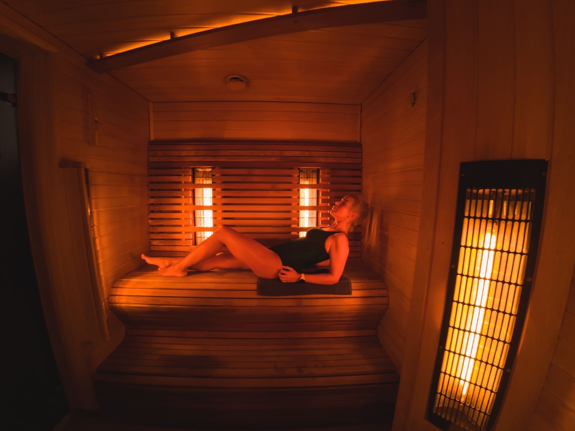 Woman relaxing in a warm, wooden infrared sauna. Warm orange light radiates throughout.