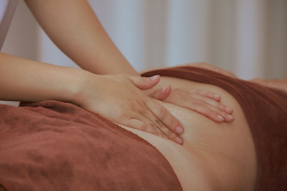 Hands massaging a person's abdomen, on a brown towel.