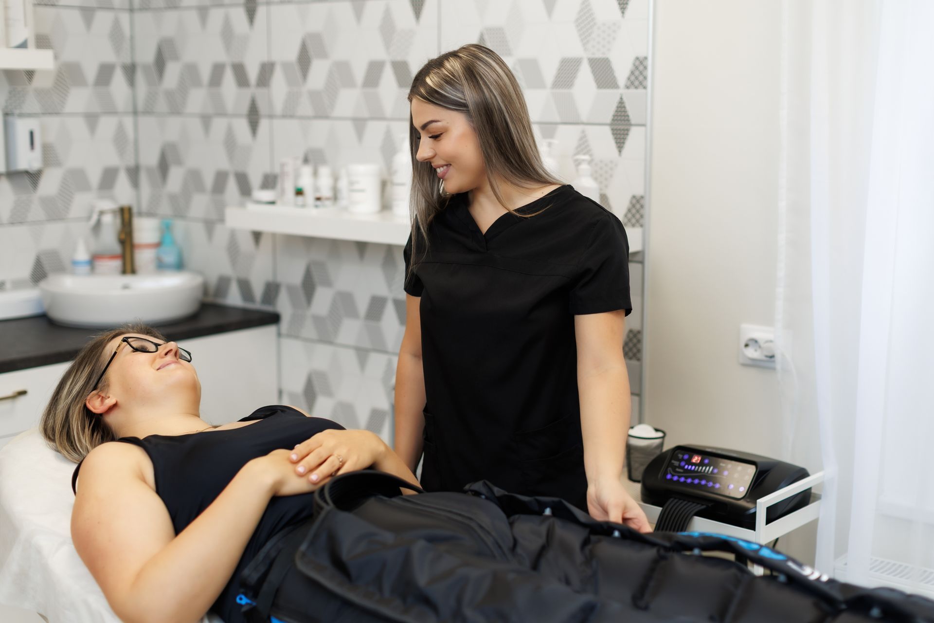 Woman receiving lymphatic drainage treatment; therapist adjusting garment, smiling. Spa setting.
