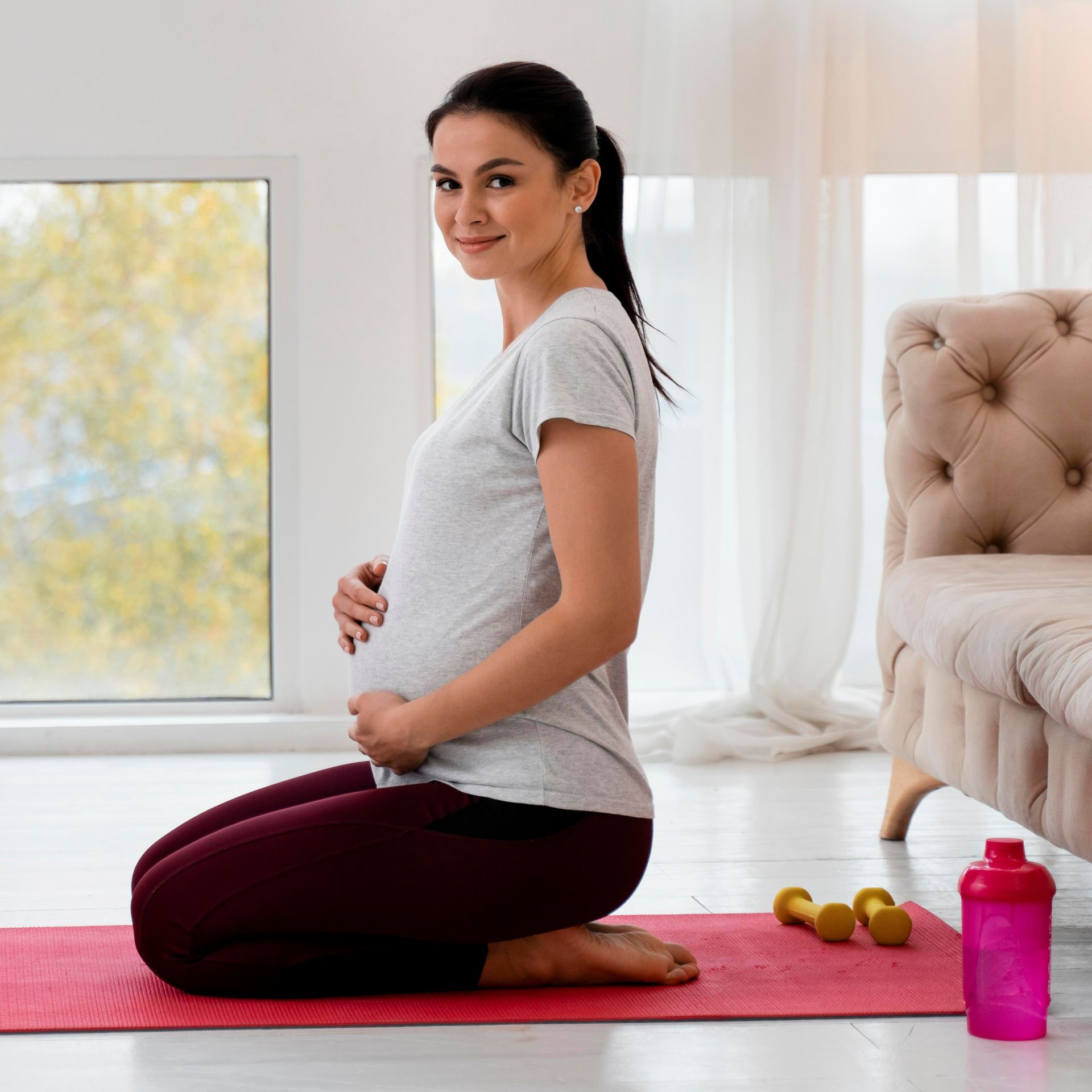 A pregnant woman is kneeling on a yoga mat