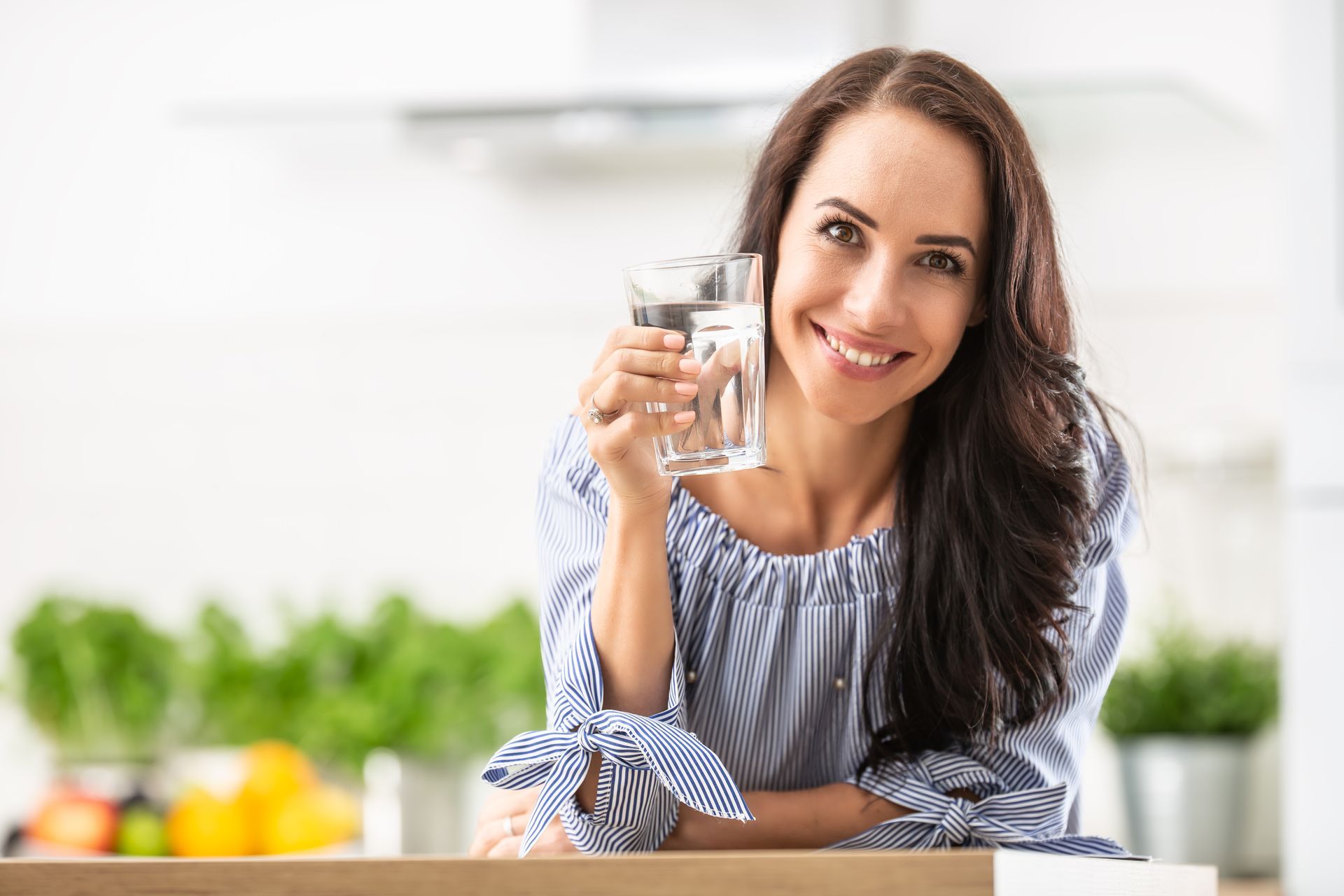 A woman is holding a glass of water in her hand in a kitchen.