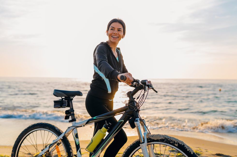 A woman is riding a bike on the beach.