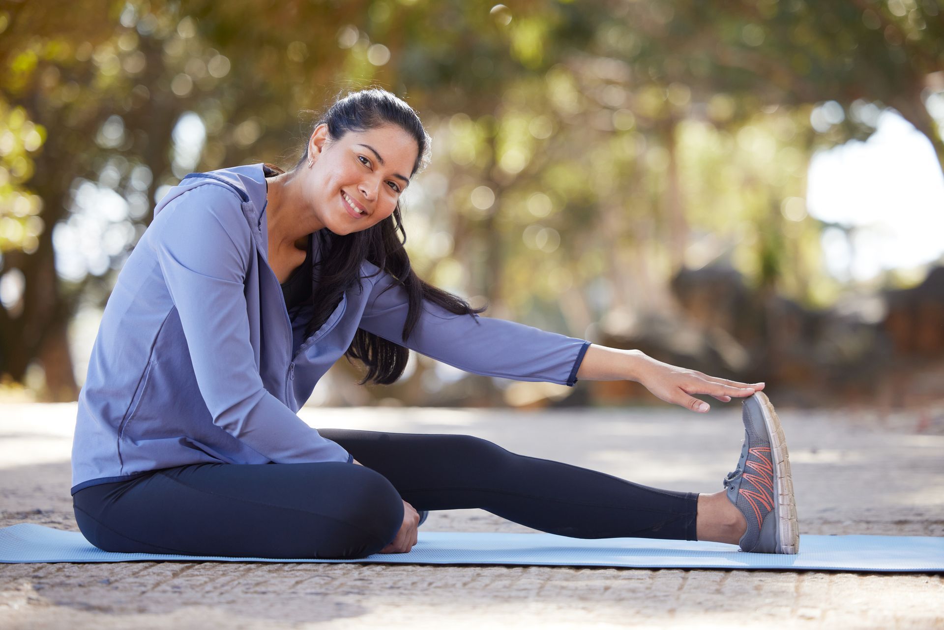 A woman is sitting on a yoga mat stretching her legs.