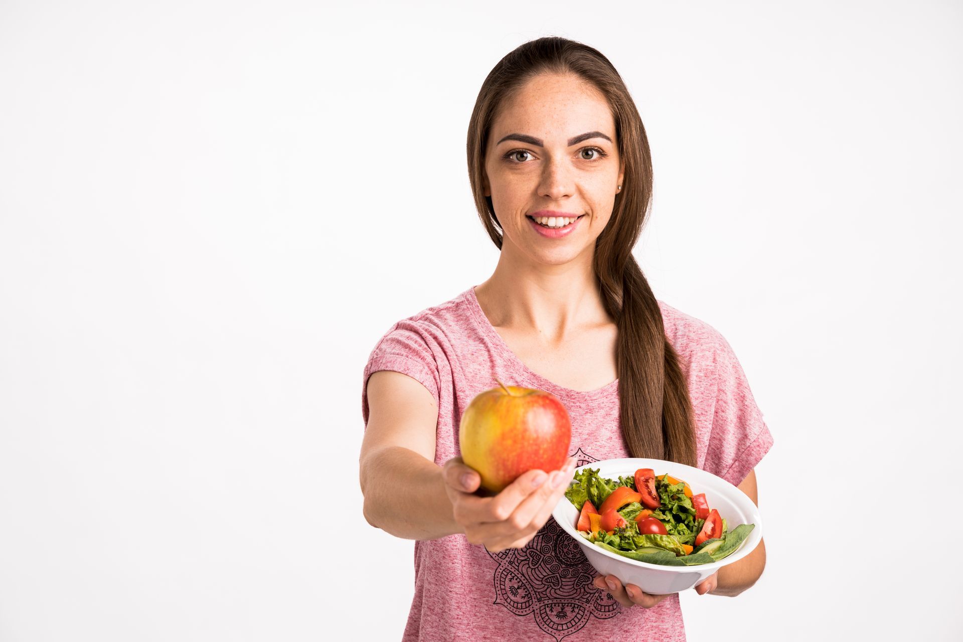 A woman is holding an apple and a bowl of salad.