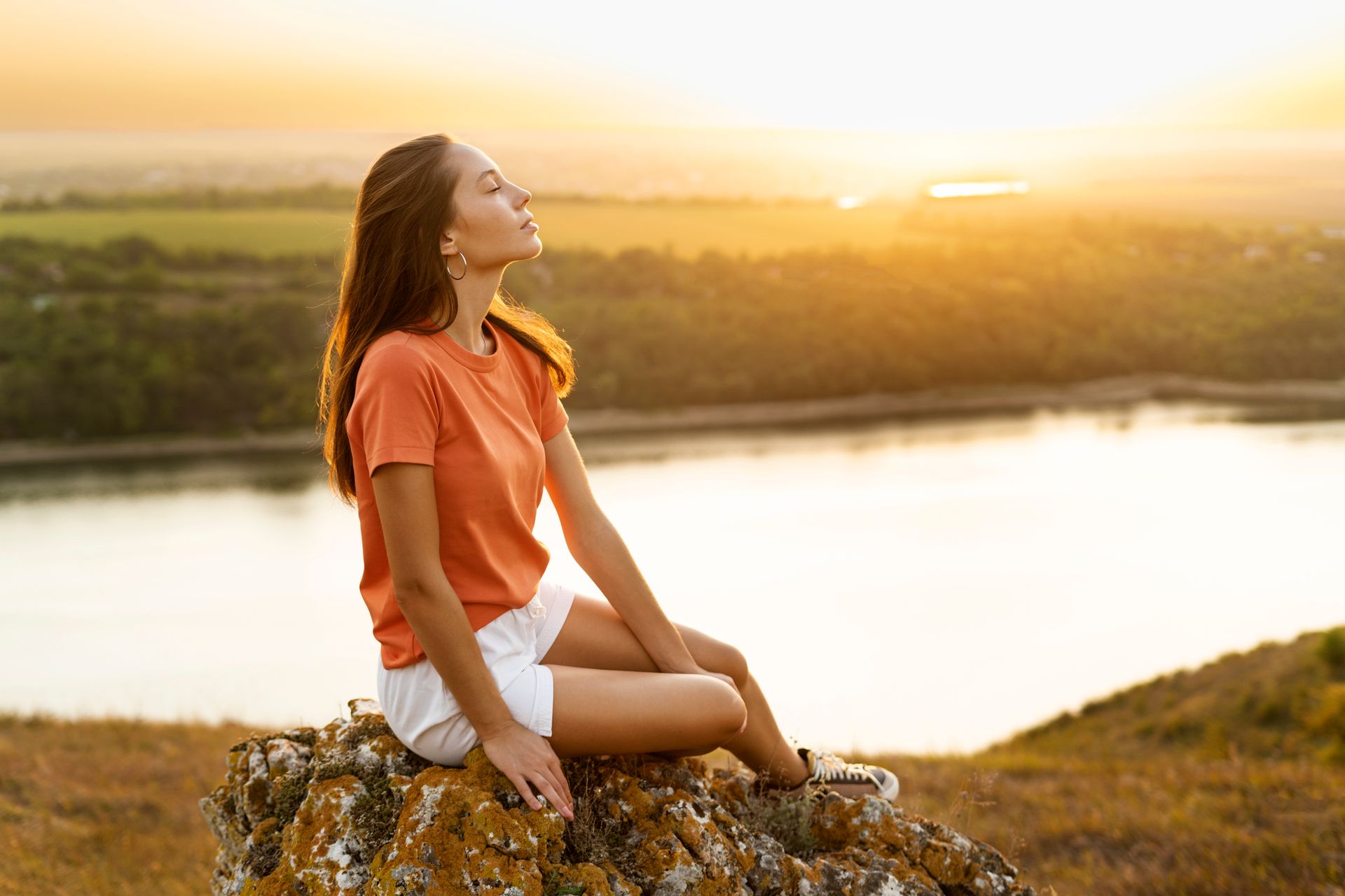 A woman is sitting on a rock overlooking a lake at sunset.