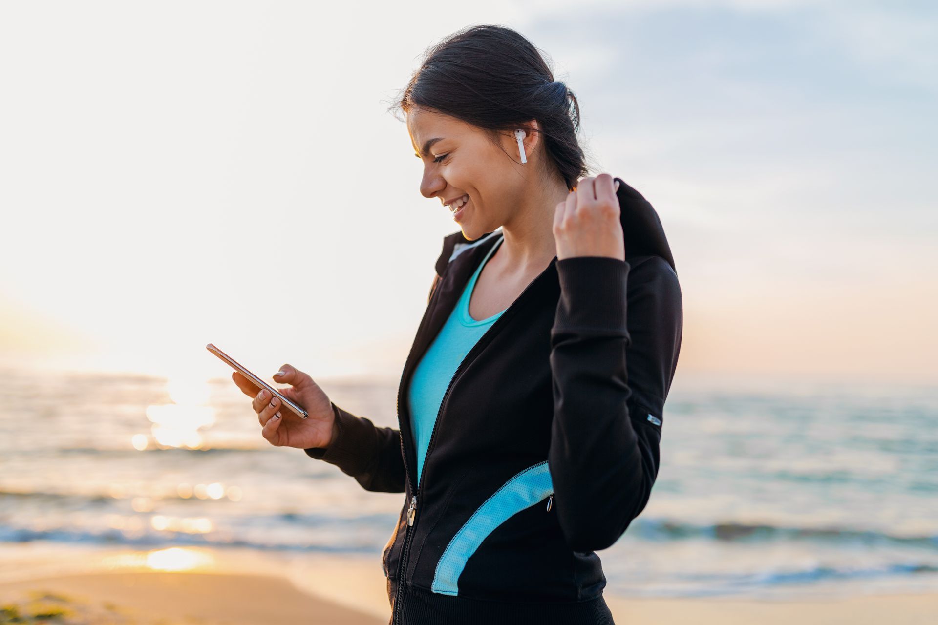 A woman is standing on the beach looking at her phone.