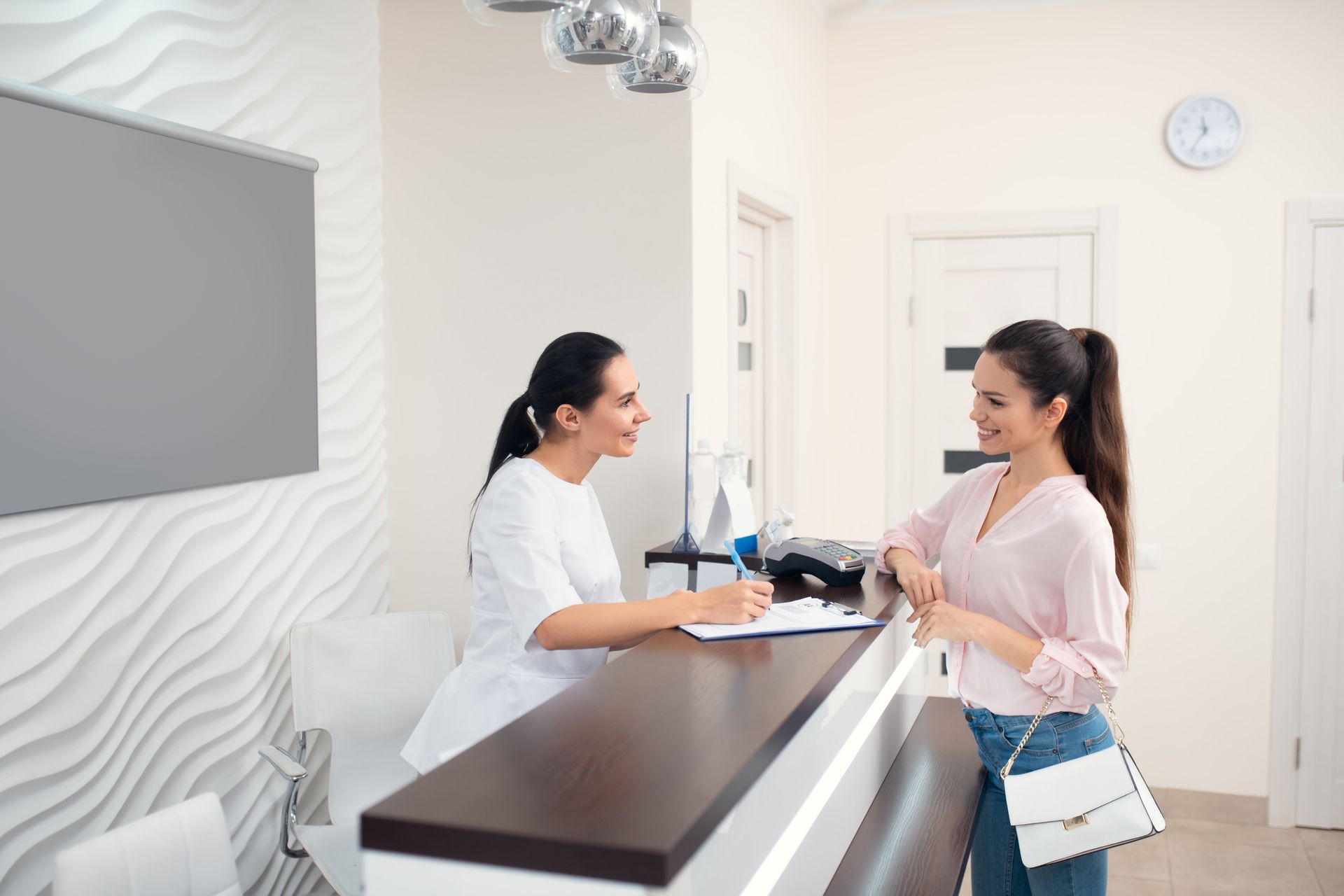 A woman is talking to a nurse at a reception desk in a hospital.