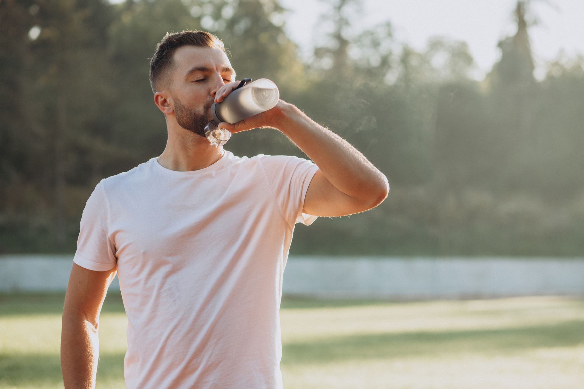 A man is drinking water from a bottle in a park.