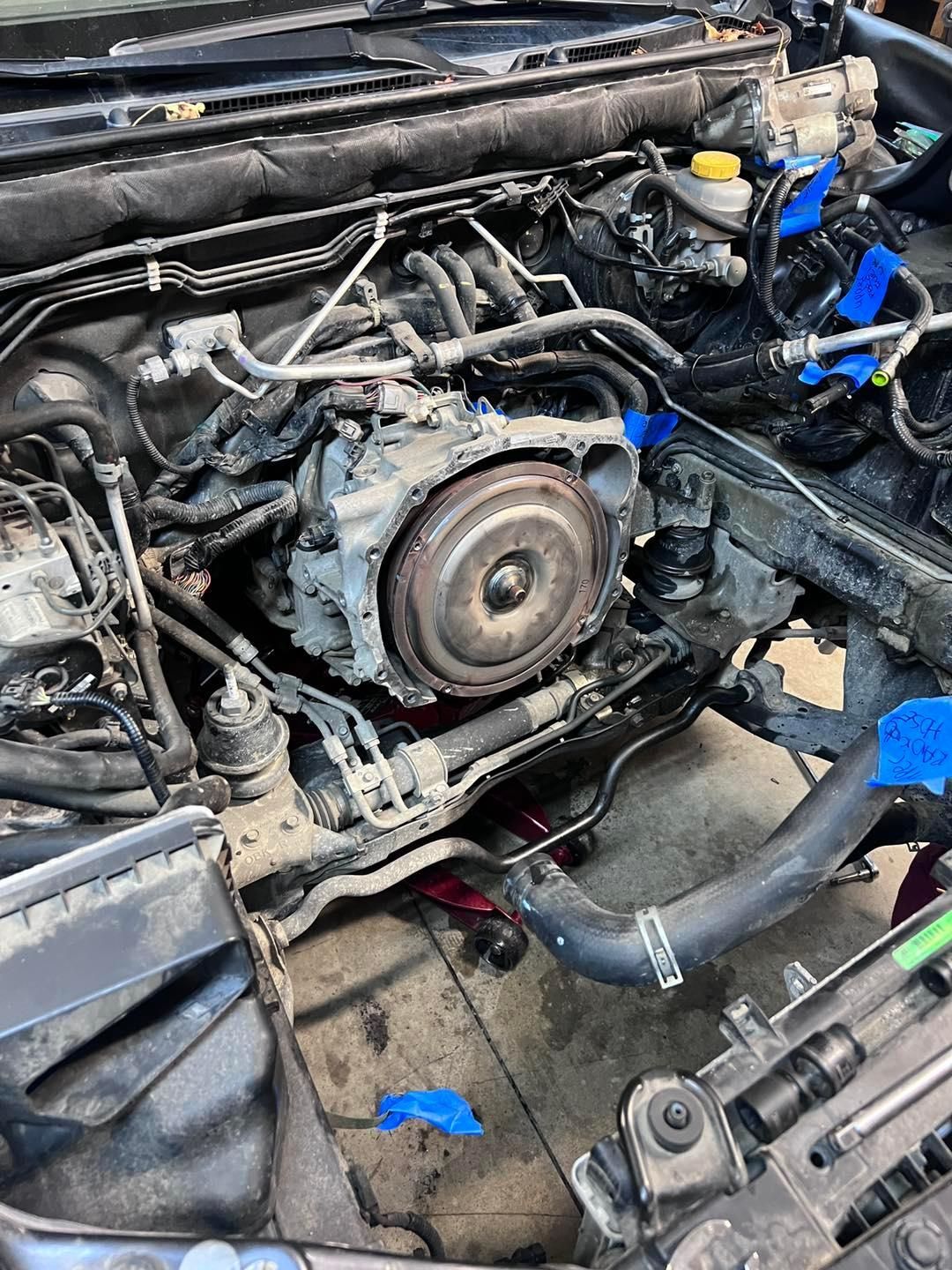 Car engine bay with removed engine, visible transmission and various components. Tools and tape visible. | Auto Medics