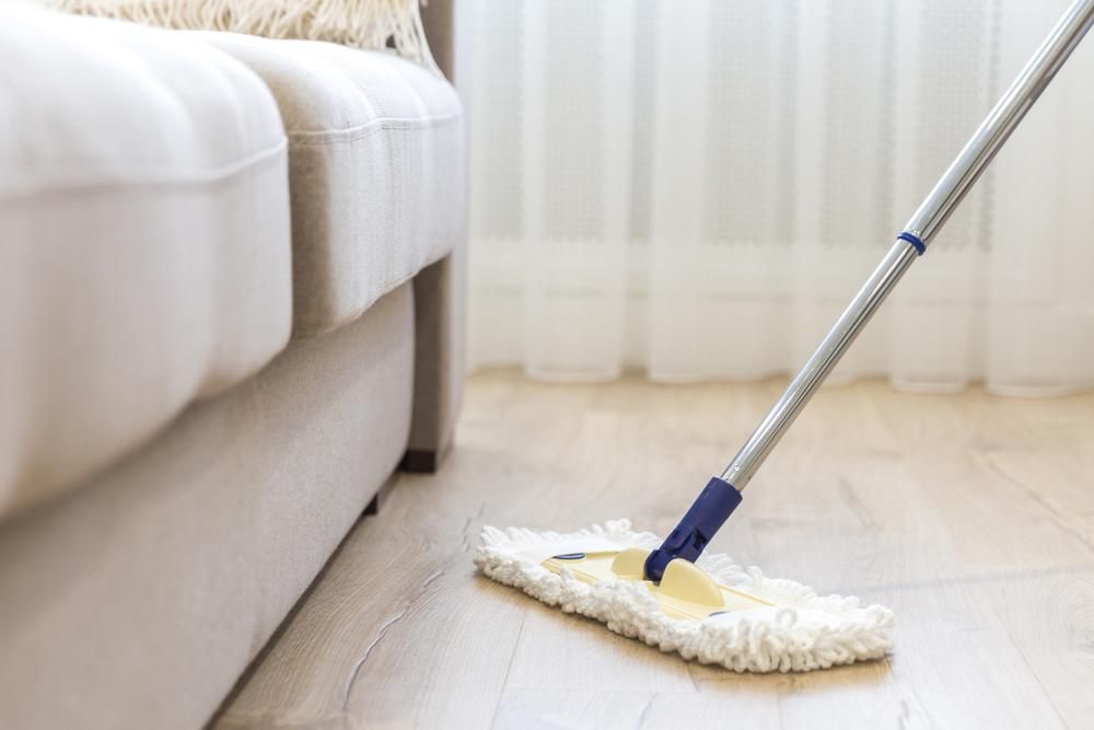 A Mop Is Being Used To Clean A Wooden Floor In A Living Room — Amy's Domestic Agency In Pimlico, QLD