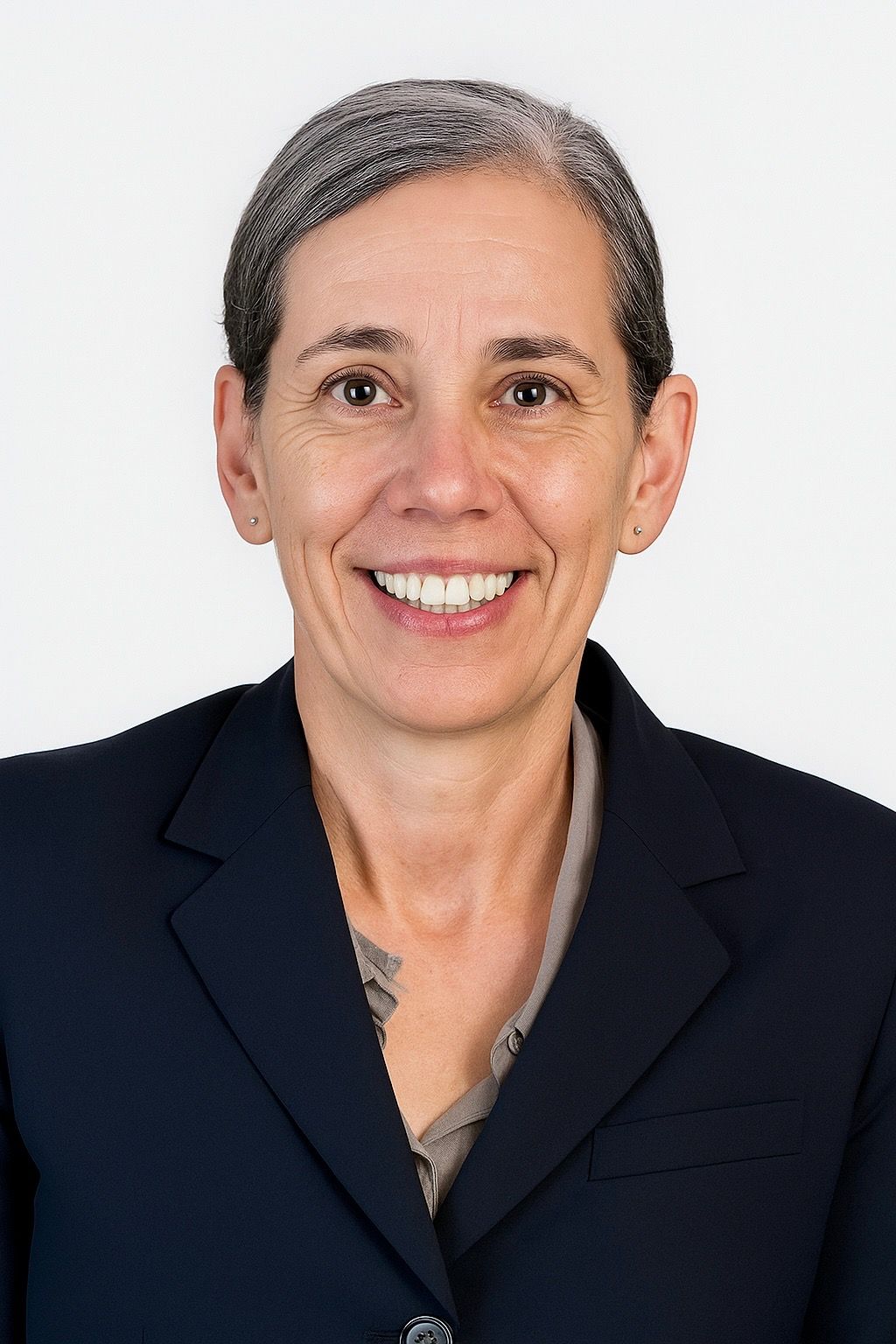 Woman in a navy blazer smiles, looking at the camera. Gray hair, neutral background.