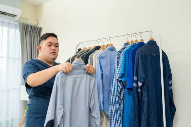 Man hanging up shirts on a clothing rack in a bedroom.