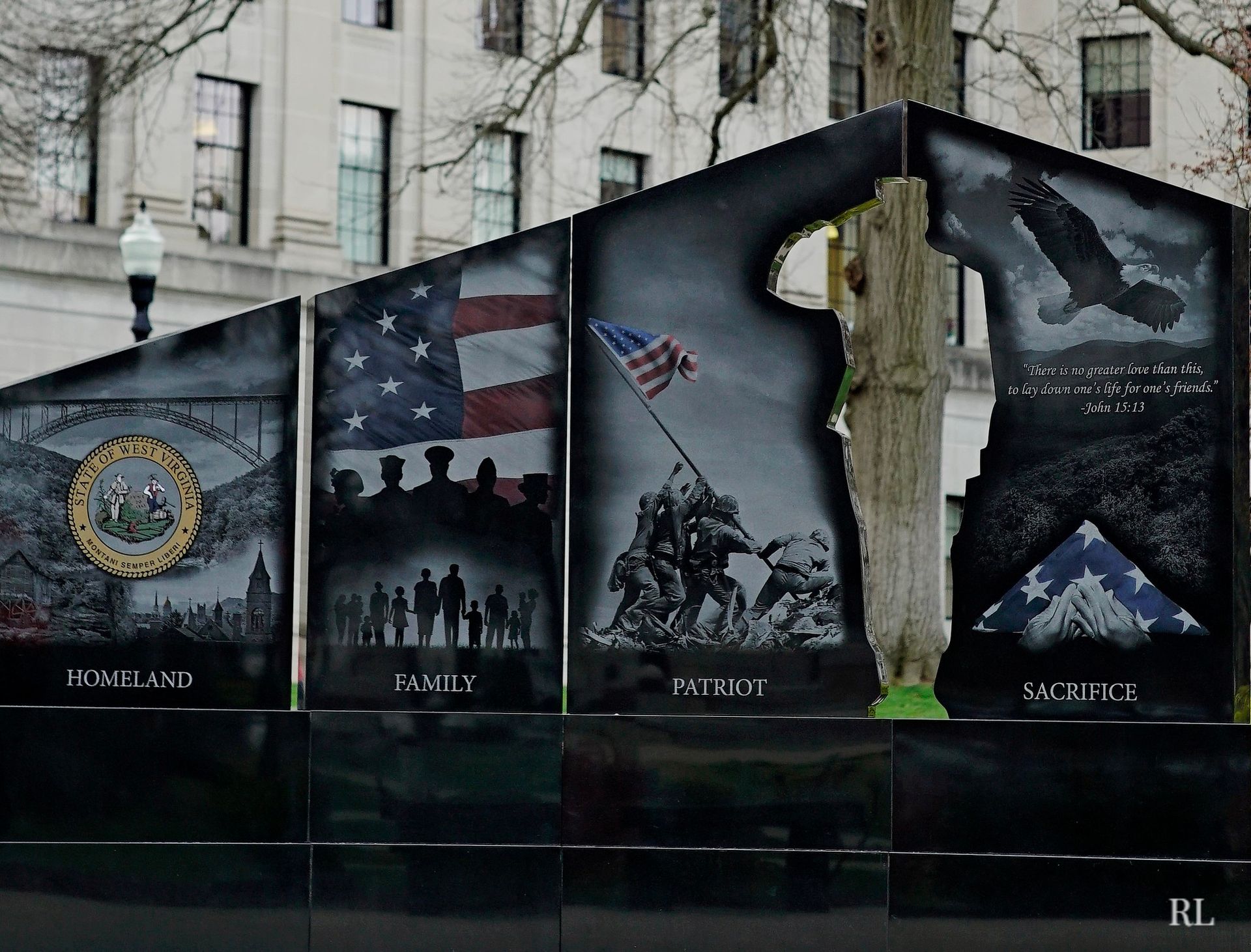 Four panels of a black granite war memorial feature etched scenes of the US flag, troops, and the Iwo Jima monument.