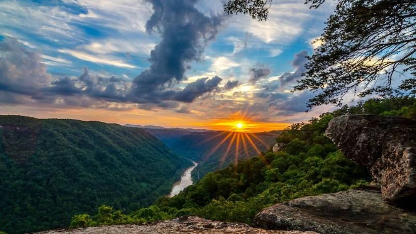 Sunset over a lush green river valley. Golden sunburst through clouds, highlighting the water.