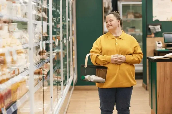 Woman with Down syndrome shopping in a grocery store, smiling, holding a basket with items.