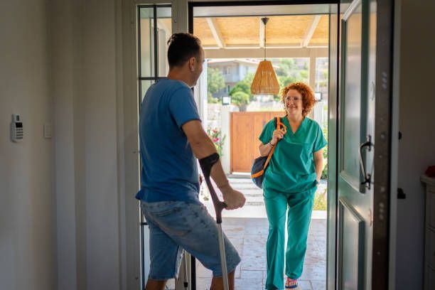 Man with crutches greets a smiling woman in scrubs at a doorway.