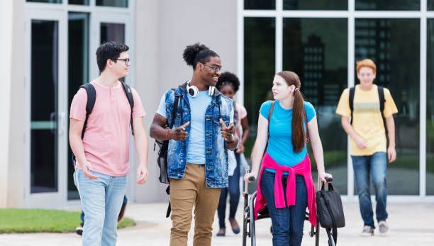 Several students walking and talking outside a building. One has a backpack and talks animatedly.