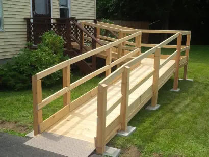 Wooden wheelchair ramp leading to a house, built on a green lawn.