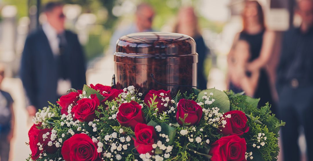 A urn is surrounded by red roses and baby 's breath at a funeral.