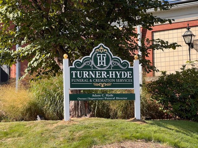 A sign for turner hyde funeral and cremation services is sitting on top of a lush green lawn.