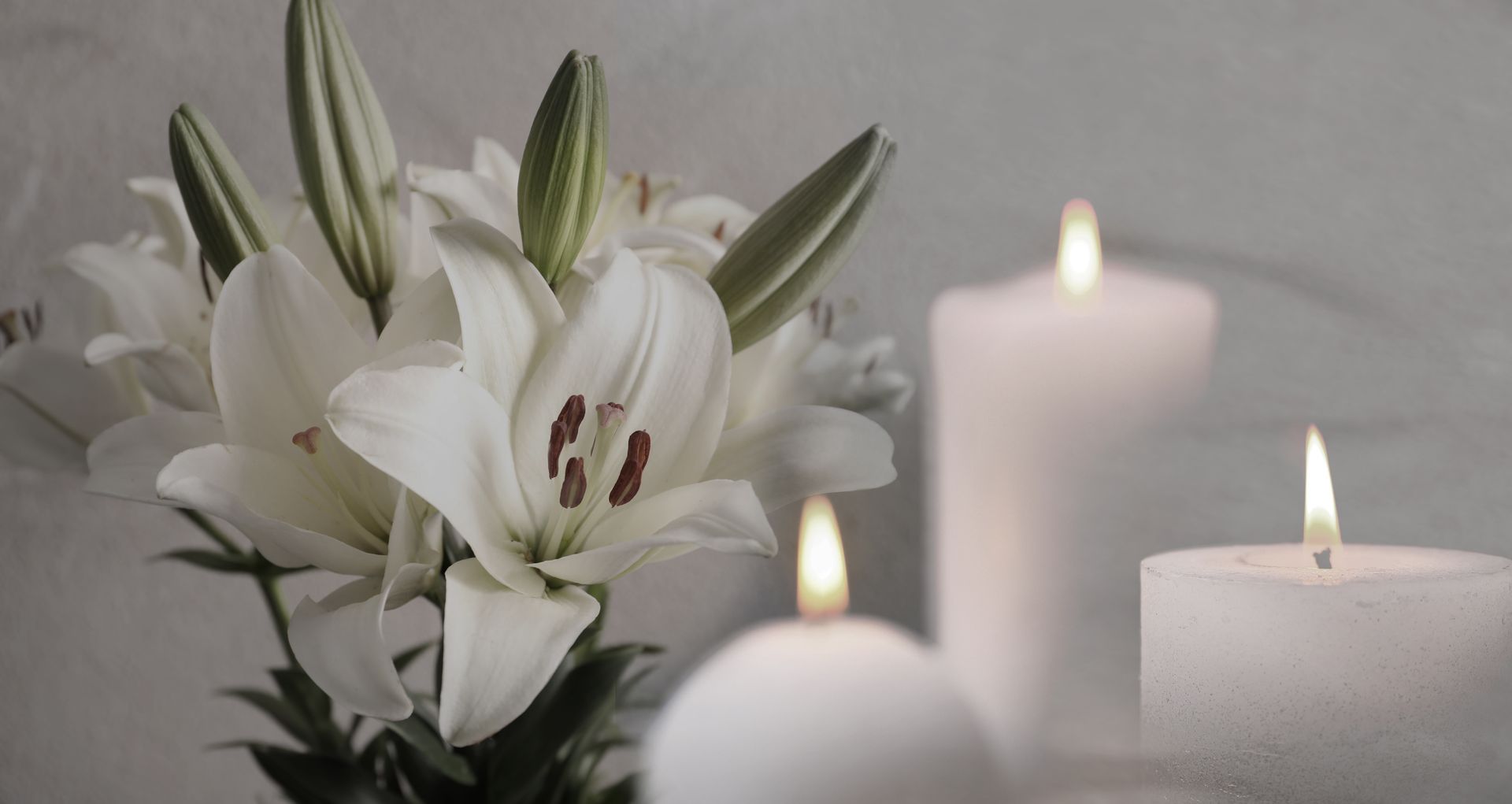 A bouquet of white lilies sitting next to three lit candles.