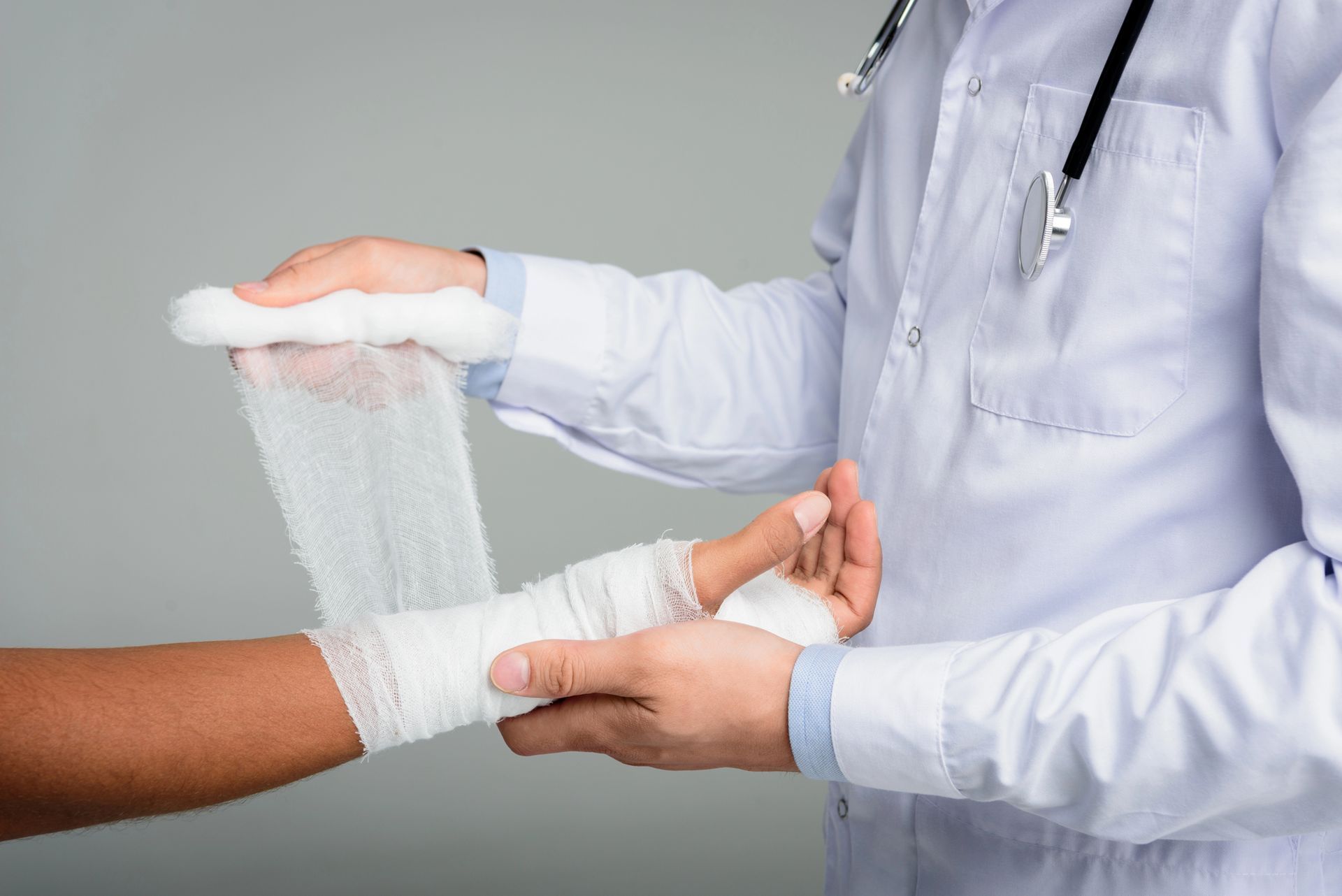 Doctor bandaging a patient’s forearm with a white gauze wrap in a clinical setting