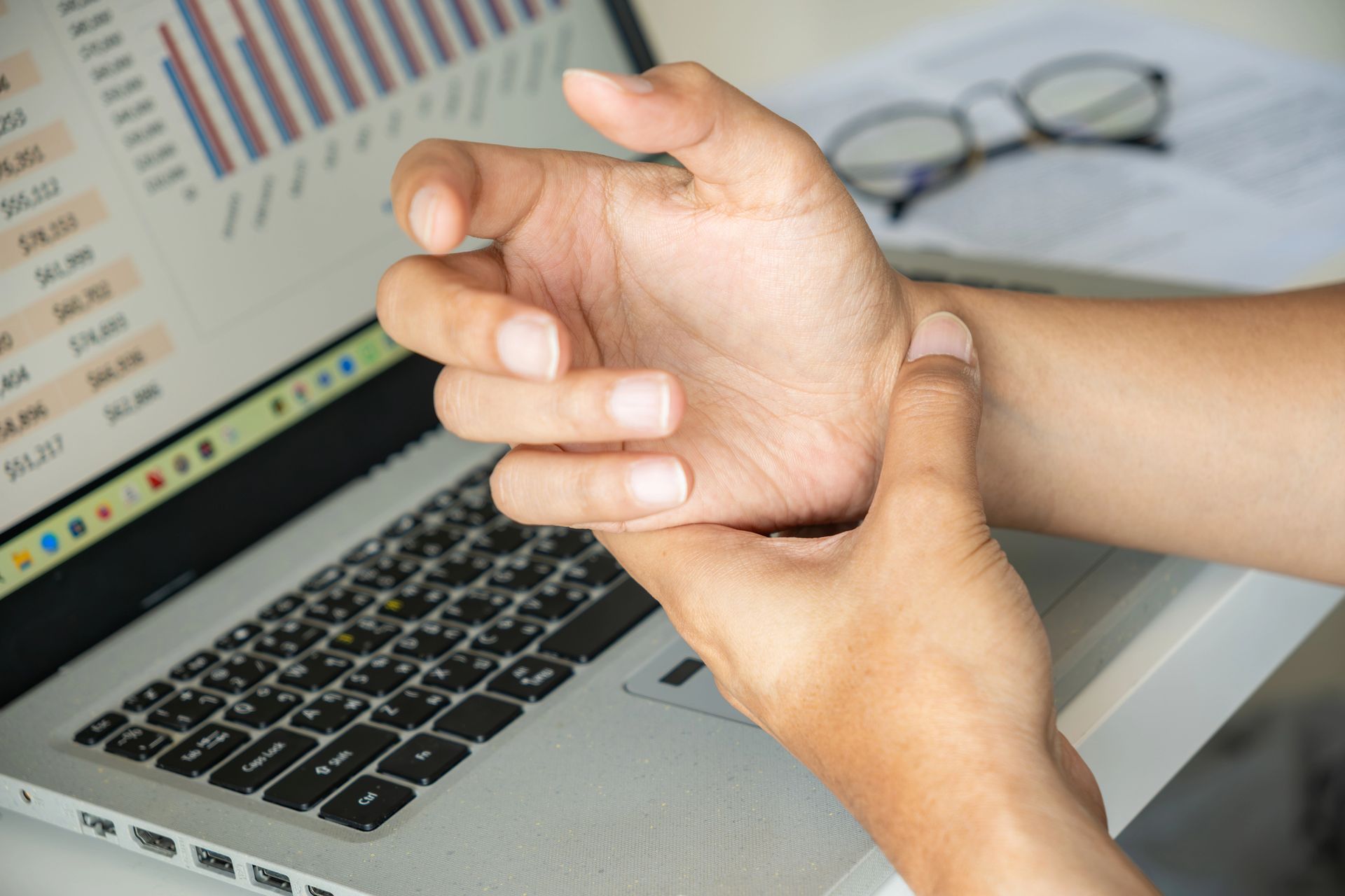 Person holding wrist in pain near laptop.