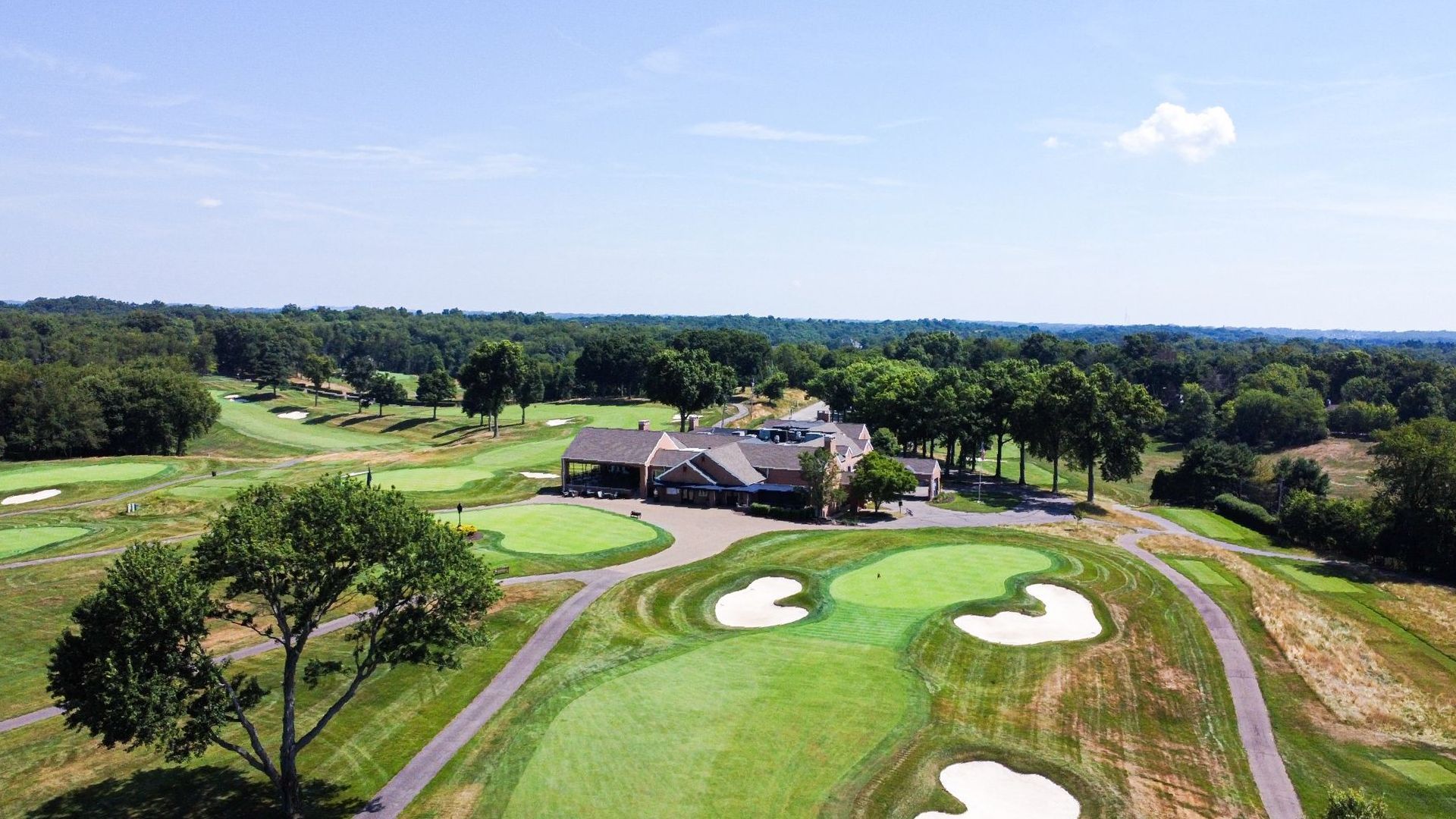 Aerial view of a golf course with a clubhouse in the center and fairways and trees surrounding.