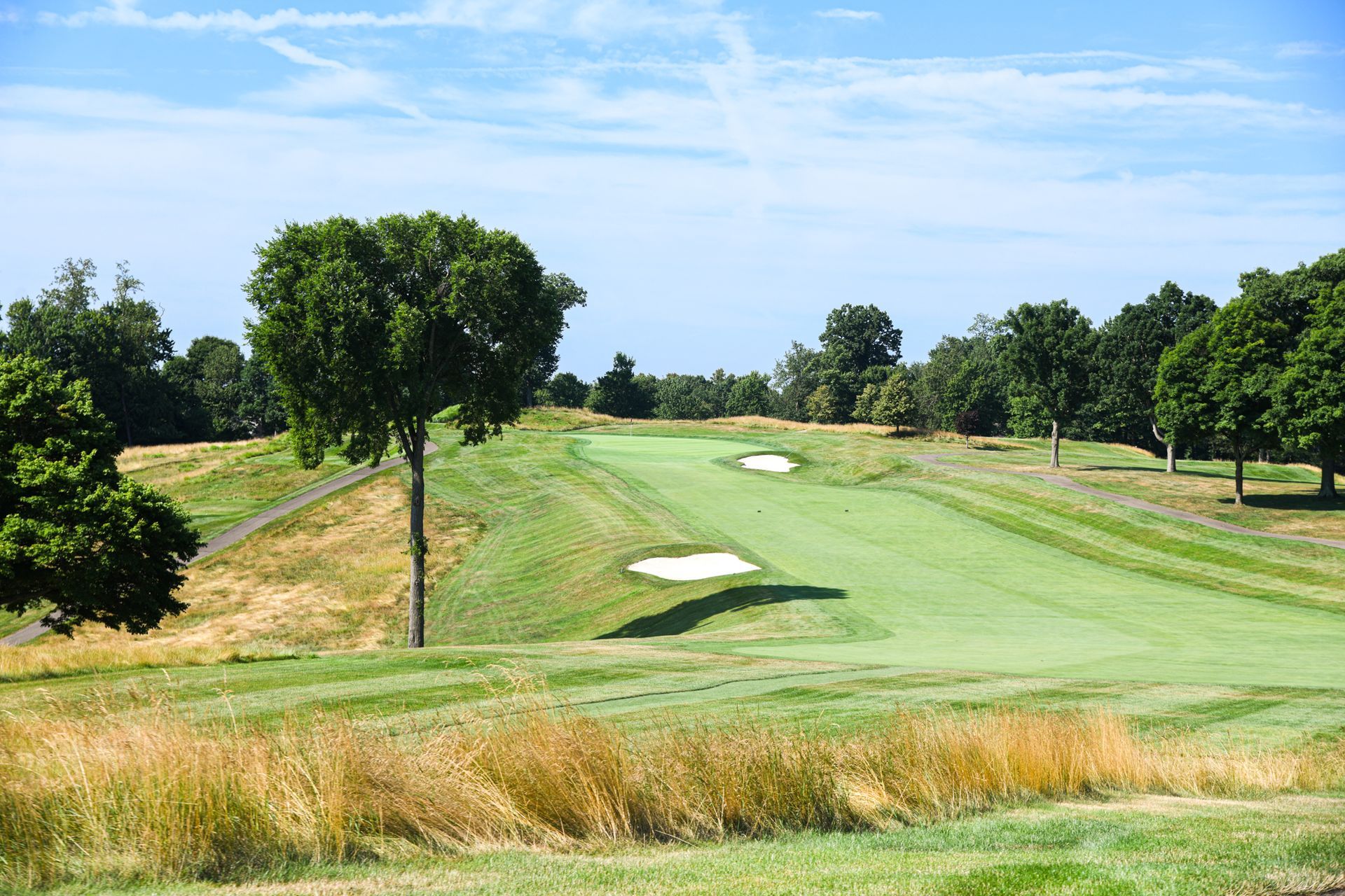 Golf course fairway with green grass and sand bunkers under a blue sky.