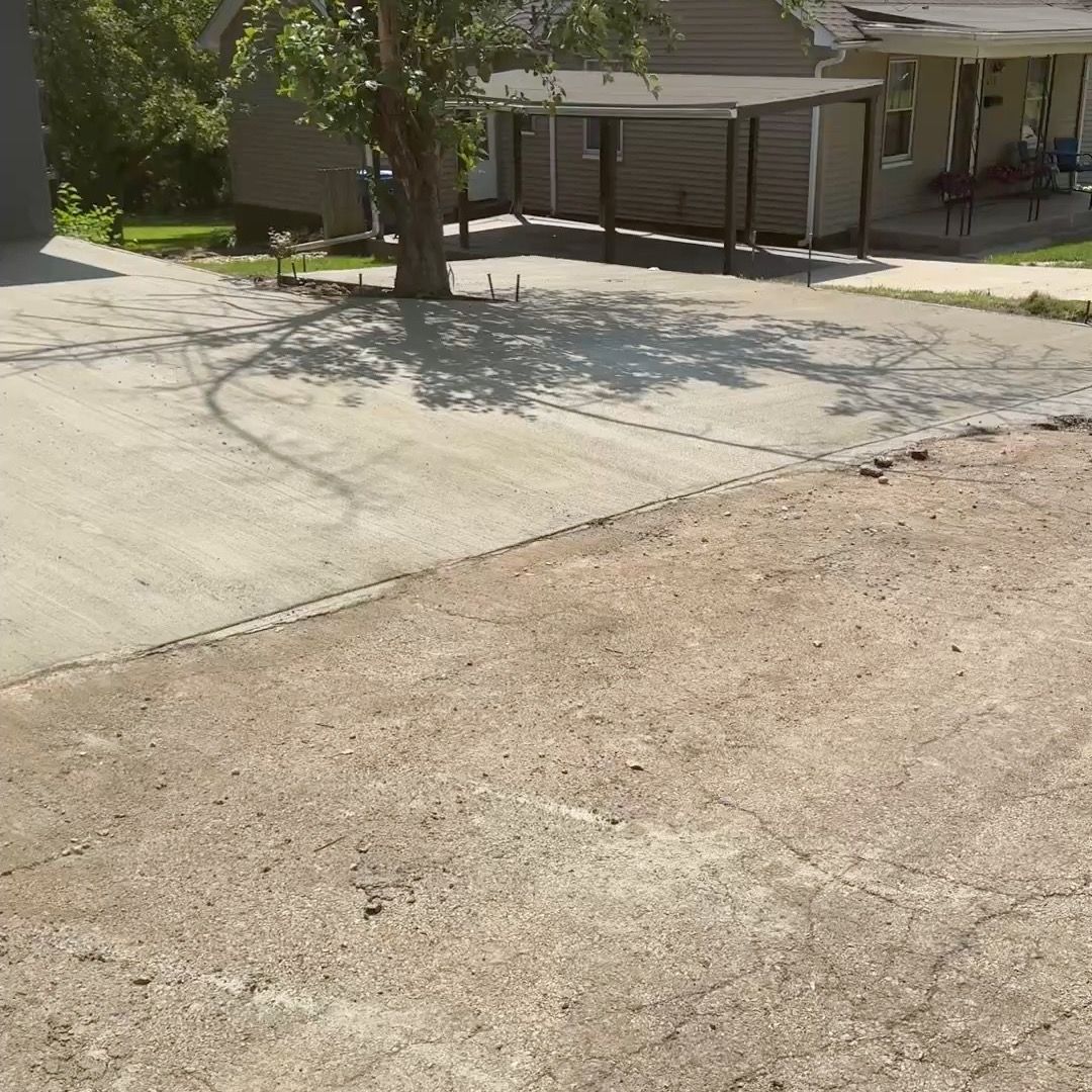 A concrete driveway leading to a house with a tree in the middle of it.