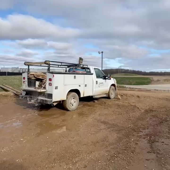 A white utility truck is parked in a muddy field.