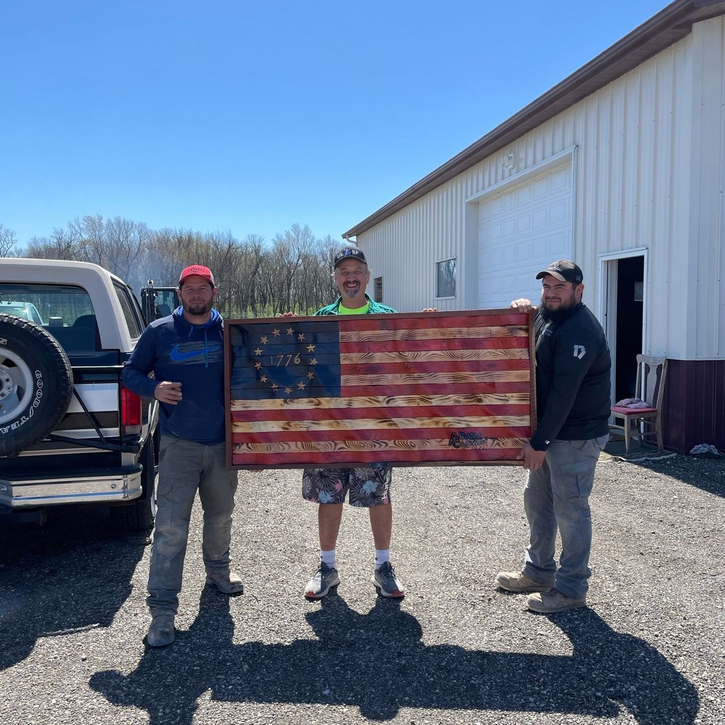 Three men holding a wooden american flag in a parking lot