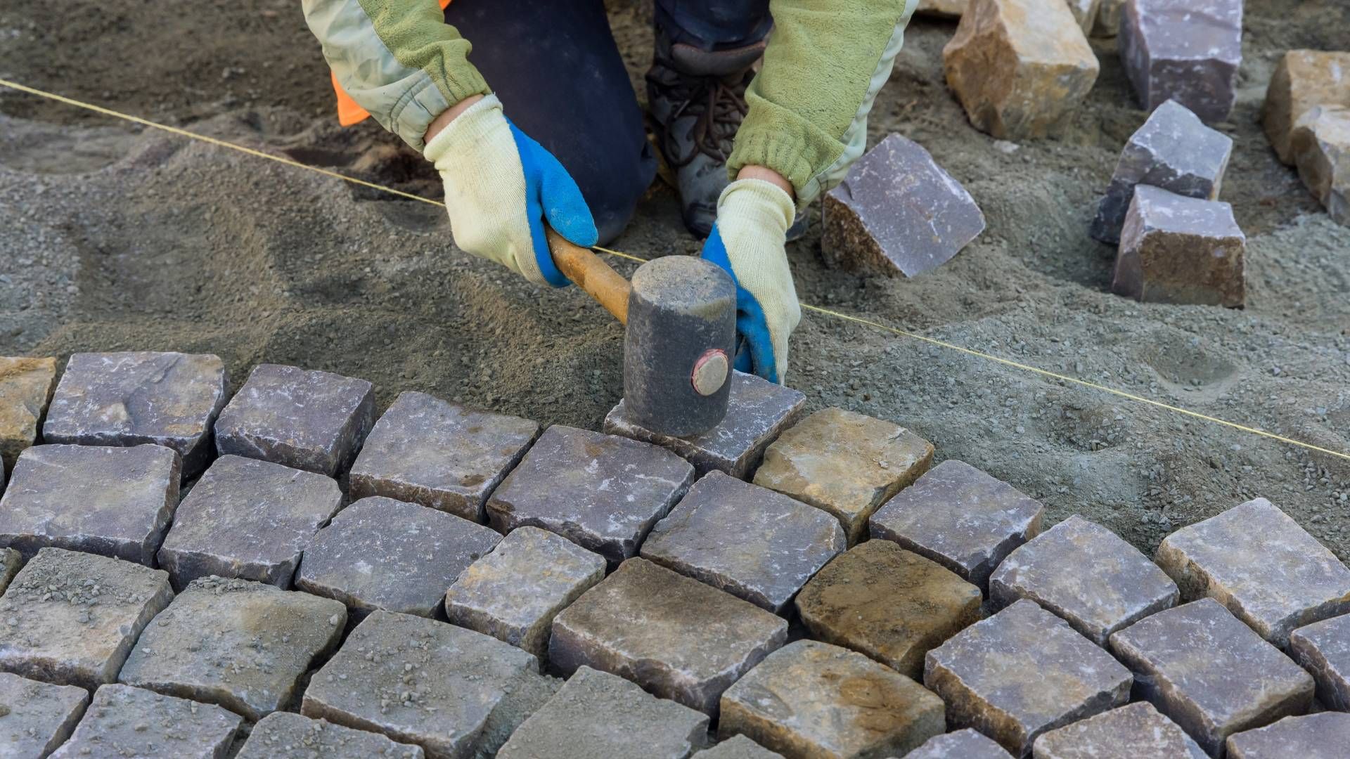 A person is laying bricks on the ground with a hammer.
