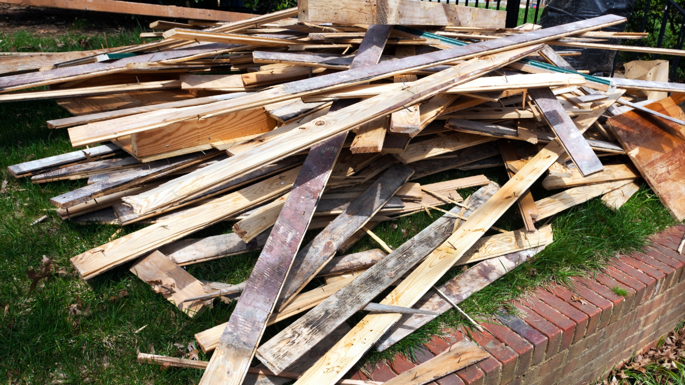 Pile of wooden planks on grass next to a brick border.