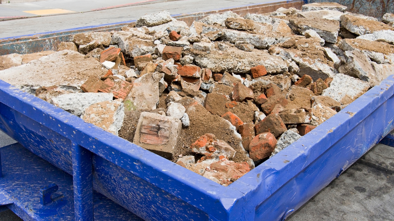 Blue dumpster filled with construction debris, including bricks and concrete.