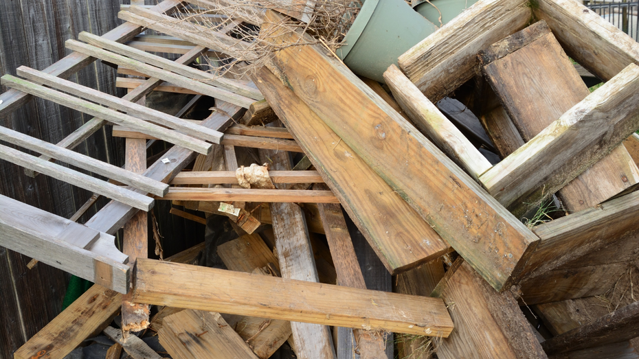 Pile of weathered wood scraps, including planks and a ladder, outdoors.