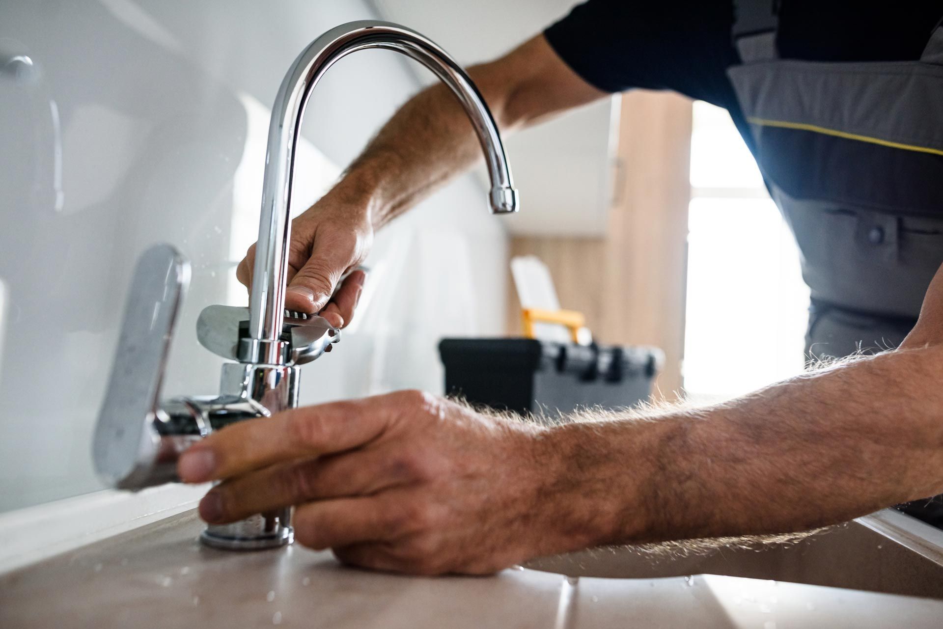 Close-up of a plumber installing a kitchen faucet, adjusting fittings at the sink with tools.