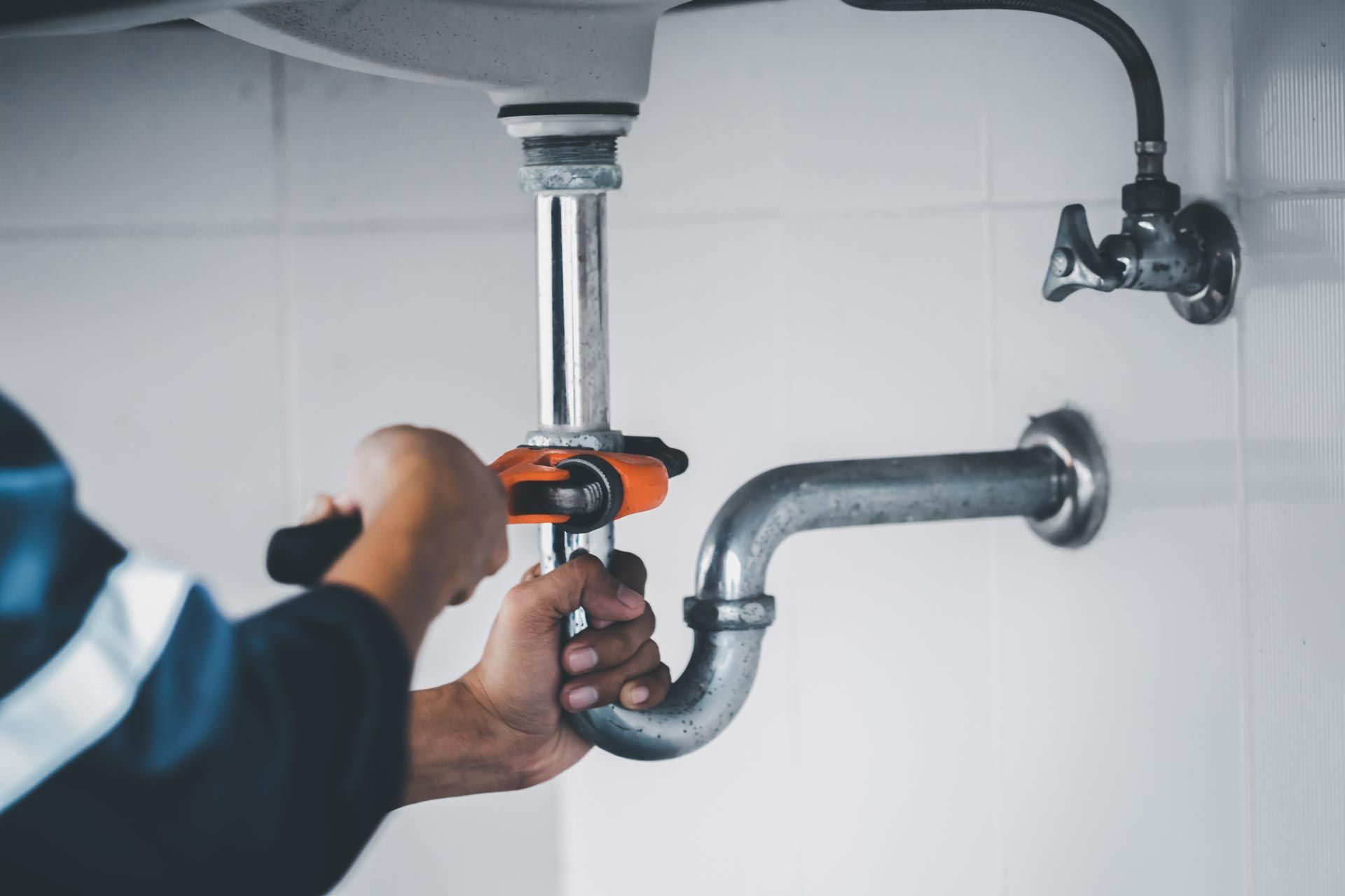 Close-up of hands tightening a sink drain pipe with a wrench beneath a bathroom sink.