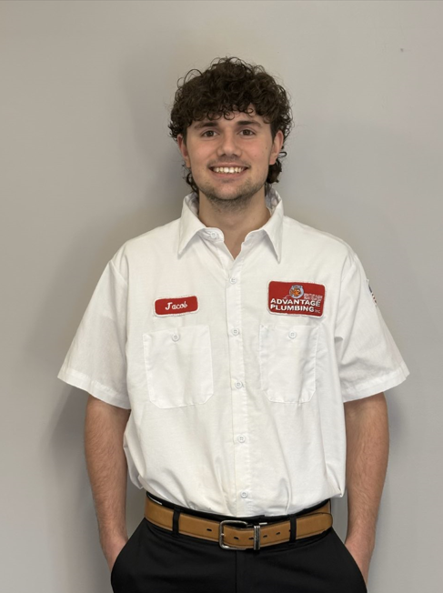 Man in white shirt with name tag and logo, hands in pockets, smiling.