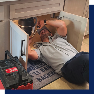 Plumber repairing garbage disposal under kitchen sink.