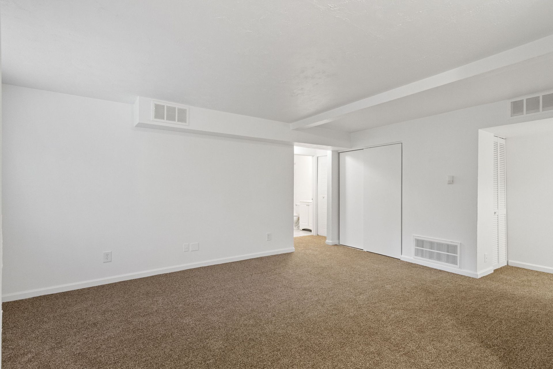 Empty room with beige carpet, white walls and ceiling, and a closed white door.