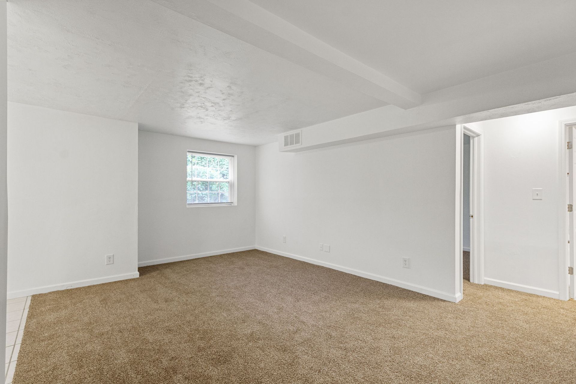 Empty room with beige carpet, white walls and ceiling, small window, and doorway.