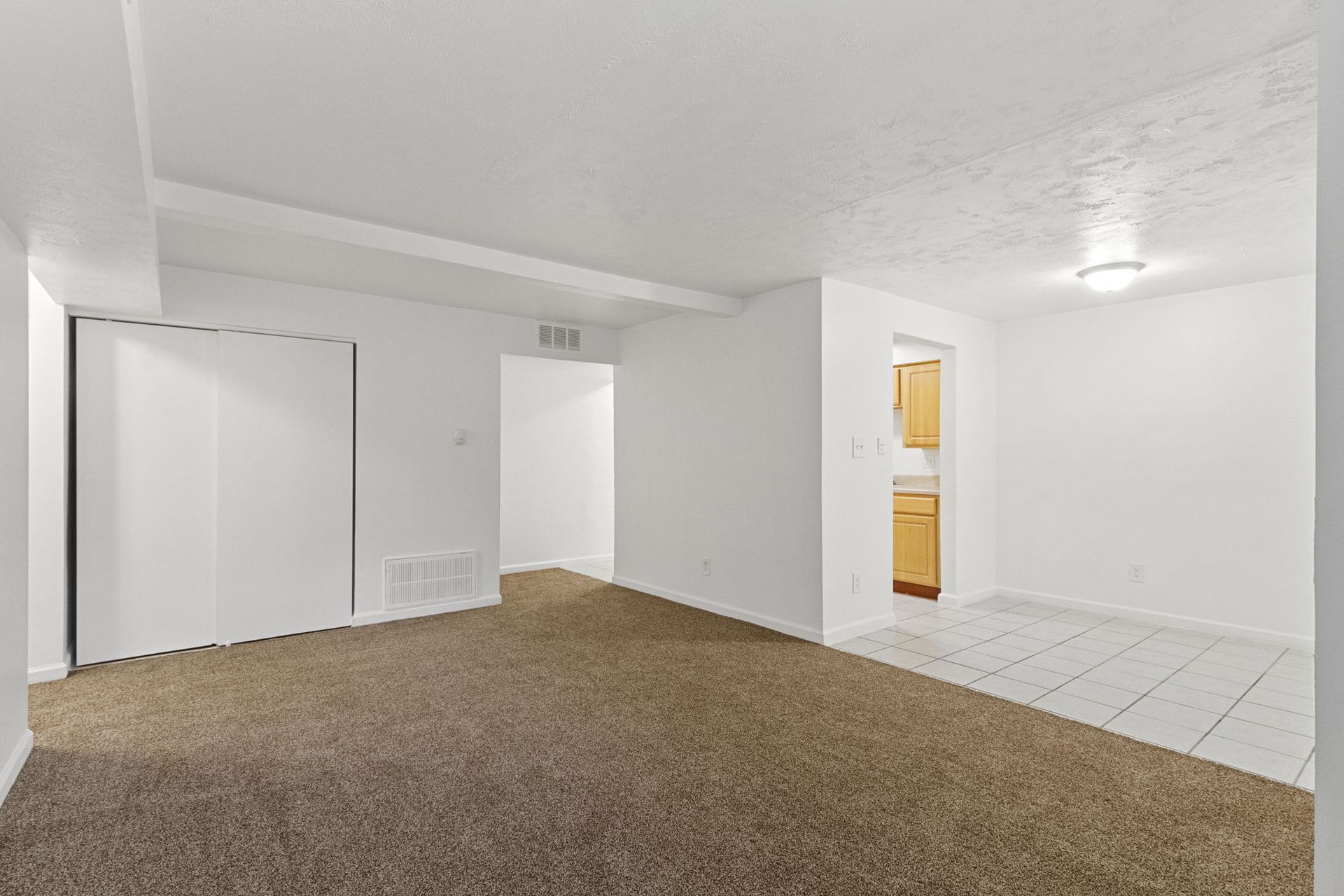Empty apartment interior, brown carpet, white walls, a closet, and a glimpse of the kitchen.